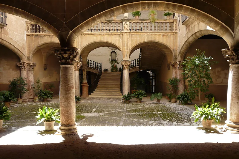 Courtyard with stone columns, arches and plants in sunlight