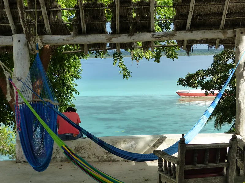 Hammocks under a palm roof with a view of a turquoise sea